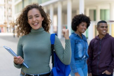 Cheering german female student with backpack and group of international students outdoor in city in summer