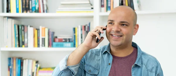 Laughing bald man talking at mobile phone indoors at home