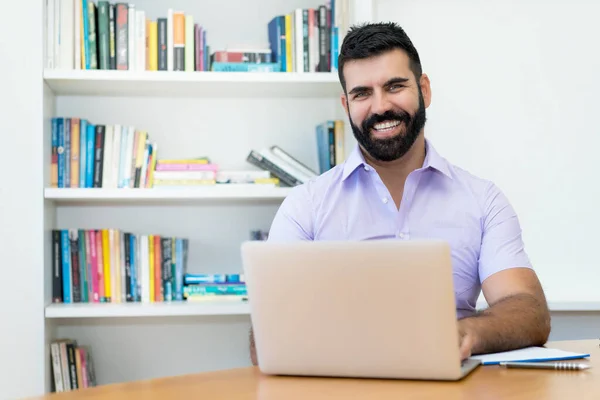 Laughing hispanic businessman with beard working at computer at desk at office