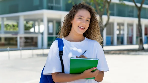 Happy german female student with backpack and paperwork outdoor in city