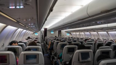 Yolcu koltuğu, koltuklarda oturan yolcuların olduğu uçağın içi ve arka planda koridorda yürüyen hostes. Seçici Odaklanma