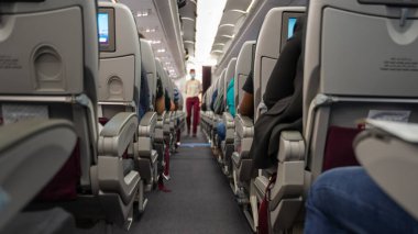 Yolcu koltuğu, koltuklarda oturan yolcuların olduğu uçağın içi ve arka planda koridorda yürüyen hostes. Seçici Odaklanma