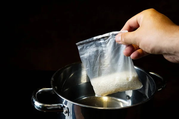 Boiling rice in portion bag. A bag of white, cooked rice is held with a hand in front of a dark background. — 스톡 사진
