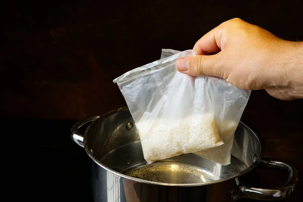 Boiling rice in portion bag. A bag of white, cooked rice is held with a hand in front of a dark background. — Fotografia de Stock