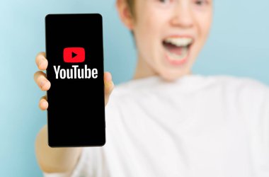 Şubat 2022 - Tallinn, Estonya. Akıllı telefonlu ve Youtube uygulamasının logosunu gösteren odaklanmamış mutlu çocuk.