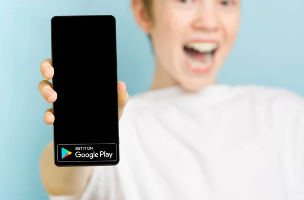 Fevereiro de 2022 - Tallinn, Estónia. Menino sorridente feliz desfocado com smartphone mostrando o logotipo do aplicativo Google Play Market — Fotografia de Stock