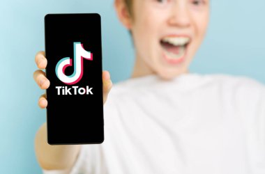 Şubat 2022 - Tallinn, Estonya. Akıllı telefonlu, odaksız mutlu çocuk Toktok uygulamasının logosunu gösteriyor.