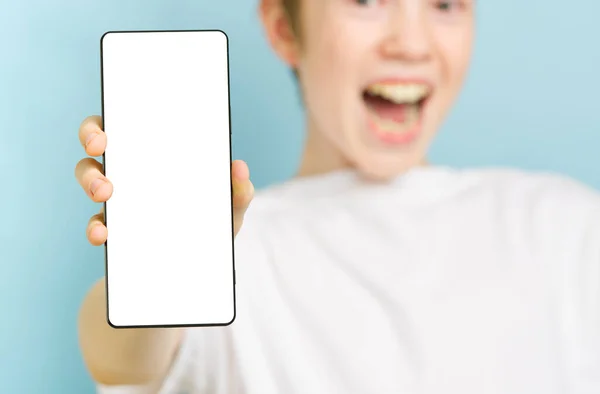 Gelukkig lachende jongen toont smartphone mockup in een blauwe achtergrond. leeg scherm voor mobiele telefoon — Stockfoto