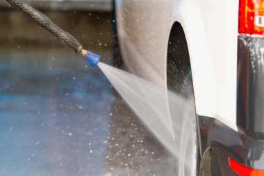 Benzin istasyonunda arabasını yıkama makinesiyle yıkayan bir adam var..