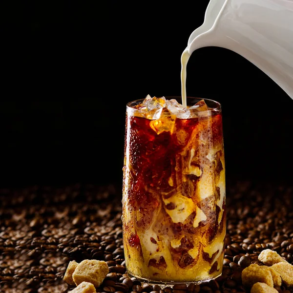 IJskoffie. Lekkere ijskoffie met melk, koude drank in glas met ijs op donkere koffie achtergrond. — Stockfoto