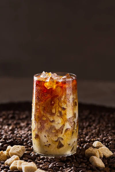Eiskaffee. Leckerer Eiskaffee mit Milch, kaltes Getränk im Glas mit Eis auf dunklem Kaffeehintergrund. — Stockfoto
