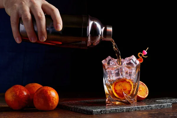 Alcohol cocktail pouring from shaker into gless with orange peel ice on stone desk. — стоковое фото