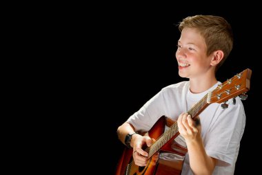 Happy boy playing on acoustic guitar. Teenager boy with classic wooden guitar. boy learning to play guitar on black background. Music education and extracurricular lessons.