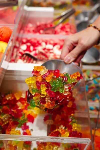 candy store. Woman hand with scoop taking colorful delicious candies on counter of shop, grocery, market, cafe. Many colorful candies on grocery stand Dessert, sale, sweet food and confectionery