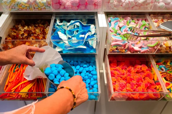candy store. Woman hand with scoop taking colorful delicious candies on counter of shop, grocery, market, cafe. Many colorful candies on grocery stand Dessert, sale, sweet food and confectionery