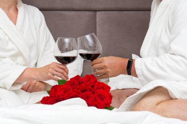 Yatakta kırmızı şaraplı mataraları tutan bir çift sevimli el. Romantizm. Rahat bir otelde, yatakta uzanmak.