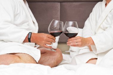 Yatakta kırmızı şaraplı mataraları tutan bir çift sevimli el. Romantizm. Rahat bir otelde, yatakta uzanmak.