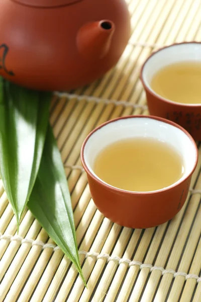 ティーポット、紅茶のカップ、パンダンの葉竹マットの上 — ストック写真
