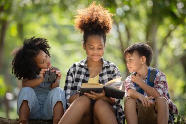 Çok ırklı çocuklar ormanı keşfederken ağaçların gölgesinde sohbet ediyorlar..