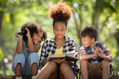 Çok ırklı çocuklar ormanı keşfederken ağaçların gölgesinde sohbet ediyorlar..