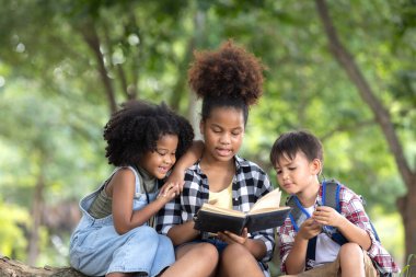 Çok ırklı çocuklar ormanı keşfederken ağaçların gölgesinde sohbet ediyorlar..