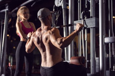 Vücut geliştiren güçlü bir sporcu spor yaparken egzersiz makinesiyle kaslarını şişiriyor..