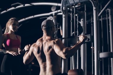 Vücut geliştiren güçlü bir sporcu spor yaparken egzersiz makinesiyle kaslarını şişiriyor..