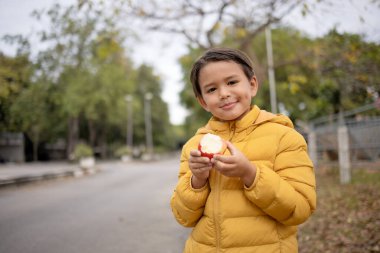 Elinde elma yediğini gösteren kışlık ceketiyle gülümseyen sevimli bir çocuk..