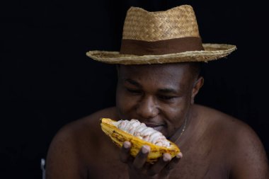Siyah Afrikalı bir çiftçi, içinde taze tohumları göstermek için kakao meyvesi tutan hasır bir şapka takıyor. Kakao meyvesi Tayland 'da bulunan tropikal egzotik meyve tarlalarıdır..
