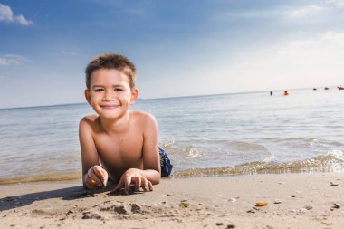 Sahilde uzanmış kameraya bakan çocuklar.
