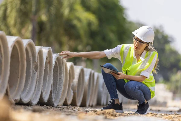 コンクリートパイプをチェックするためにタブレットを使用してハード帽子を持つ女性建設現場エンジニアの建築家の労働者 — ストック写真
