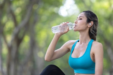 Ağaç kaplı bir patikada antrenman yaptıktan sonra şişeden su içerken gülümseyen mutlu genç bayan..