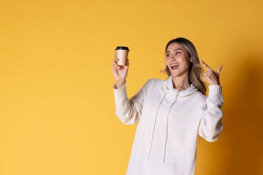 Asya 'lı sarışın, dalgalı saçlı, çekici bir genç kızın portresi. Sarı arka planda kahve için kağıt bardakları tutuyor..