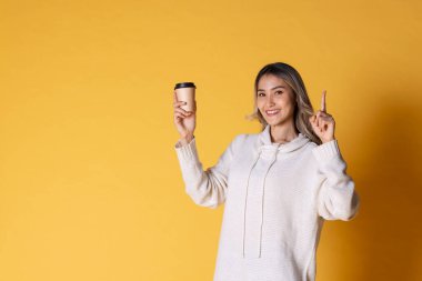 Asya 'lı sarışın, dalgalı saçlı, çekici bir genç kızın portresi. Sarı arka planda kahve için kağıt bardakları tutuyor..