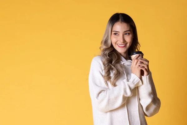 Portrait of Asia woman blond teenage girl with wavy hair looking charming holding paper disposable cup for coffee on over yellow background.