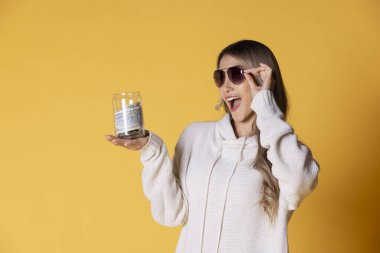 Genç Asya 'lı, güneş gözlüğü takan neşeli bir kadın. Elinde bir seyahat gezisinden arta kalan parayla dolu cam bir şişe tutuyor..