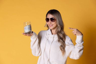 Genç Asya 'lı, güneş gözlüğü takan neşeli bir kadın. Elinde bir seyahat gezisinden arta kalan parayla dolu cam bir şişe tutuyor..