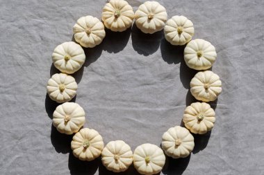 Yuvarlak sonbahar çerçevesi, beyaz balkabaklarından yapılmış doğal halkalar. Düz yerde, gri renksiz keten tekstil manzaralı. Fotokopi alanı ile arkaplanı düşür. Doğal güneş ışığı, güçlü gölgeler..