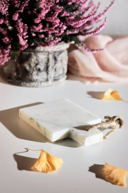 Kozmetik ürünler, atıştırmalıklar veya tatlılar için sonbahar arka planı. Ürün için yeri olan mermer kaide. Mermer kesim tahtası, pembe kenevir kabı ve kuru sarı ginkgo yaprakları. Düşen maket, taş podyum.