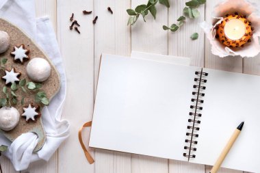 Kışlık defter, okaliptüs dalları, doğal portakallı çay ışığı ve seramik tahtada zencefilli kurabiye. Düz yatıyordu, beyaz kırsal ahşap tahtaların üstünde üst görünümü vardı, kendi kendine yapılmış bir masa..