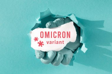 Omicron varyantını koronavirüs siluetiyle yaz. Eldivenle kağıt deliğinde Corona virüsünün yeni adı olan yırtık bir kağıt parçası tutuyordu.. 