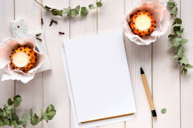 Kışlık defter, okaliptüs dalları, doğal portakallı çay ışığı ve seramik tahtada zencefilli kurabiye. Düz yatıyordu, beyaz kırsal ahşap tahtaların üstünde üst görünümü vardı, kendi kendine yapılmış bir masa..