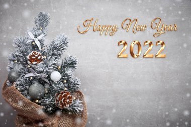 2022 Mutlu Yıllar mesajı. Kırmızı süs eşyalarıyla süslenmiş çuval bezli küçük Noel ağacı ve fotokopi alanı ile ışıktaşı arka planında böğürtlenler.