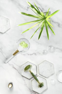 El yapımı nemlendirici ve yeşil yeşim taşlı yüz silindiri. Pamuk havlu. Egzotik okaliptüs yaprakları ve su beyaz mermer arka planda taş altıgenlerle birlikte düşer. Yüz masajı, kendi kendine yapılan kozmetikler..