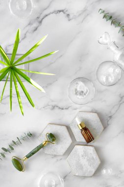 Kendi yapımı nemlendirici ve yeşil yeşim taşı yüzlü mermer altıgen. Egzotik dikişler ve okaliptüs yaprakları beyaz mermer arka planda. Yüz masajı, el yapımı kozmetik konsepti.