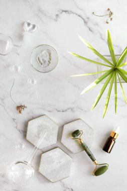 Kendi yapımı nemlendirici ve yeşil yeşim taşı yüzlü mermer altıgen. Beyaz mermer arka planda egzotik sedge su bitkisi yaprağı. Yüz masajı, el yapımı kozmetik..