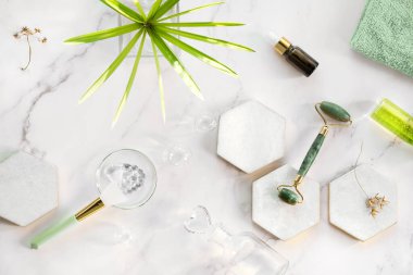 Kendi yapımı nemlendirici ve yeşil yeşim taşı yüzlü mermer altıgen. Beyaz mermer arka planda egzotik sedge su bitkisi yaprağı. Yüz masajı, el yapımı kozmetik konsepti.