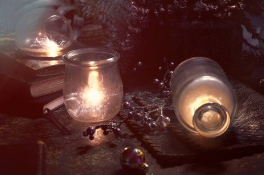 Magic lights with sparkles and orange glow in vintage glass jars. Lights and old books. Fir twigs and heather flowers. Romantic evening indoors. Wintertime, winter holidays