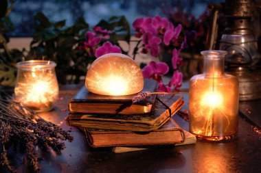 Magic lights with sparkles and orange glow in various glass jars. Wintertime with lights and old vintage books in a stack. Orchid, heather flowers. Romantic indoor background on rainy day.