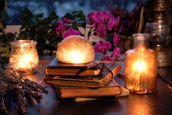 Magic lights with sparkles and orange glow in various glass jars. Wintertime with lights and old vintage books in a stack. Orchid, heather flowers. Romantic indoor background on rainy day.